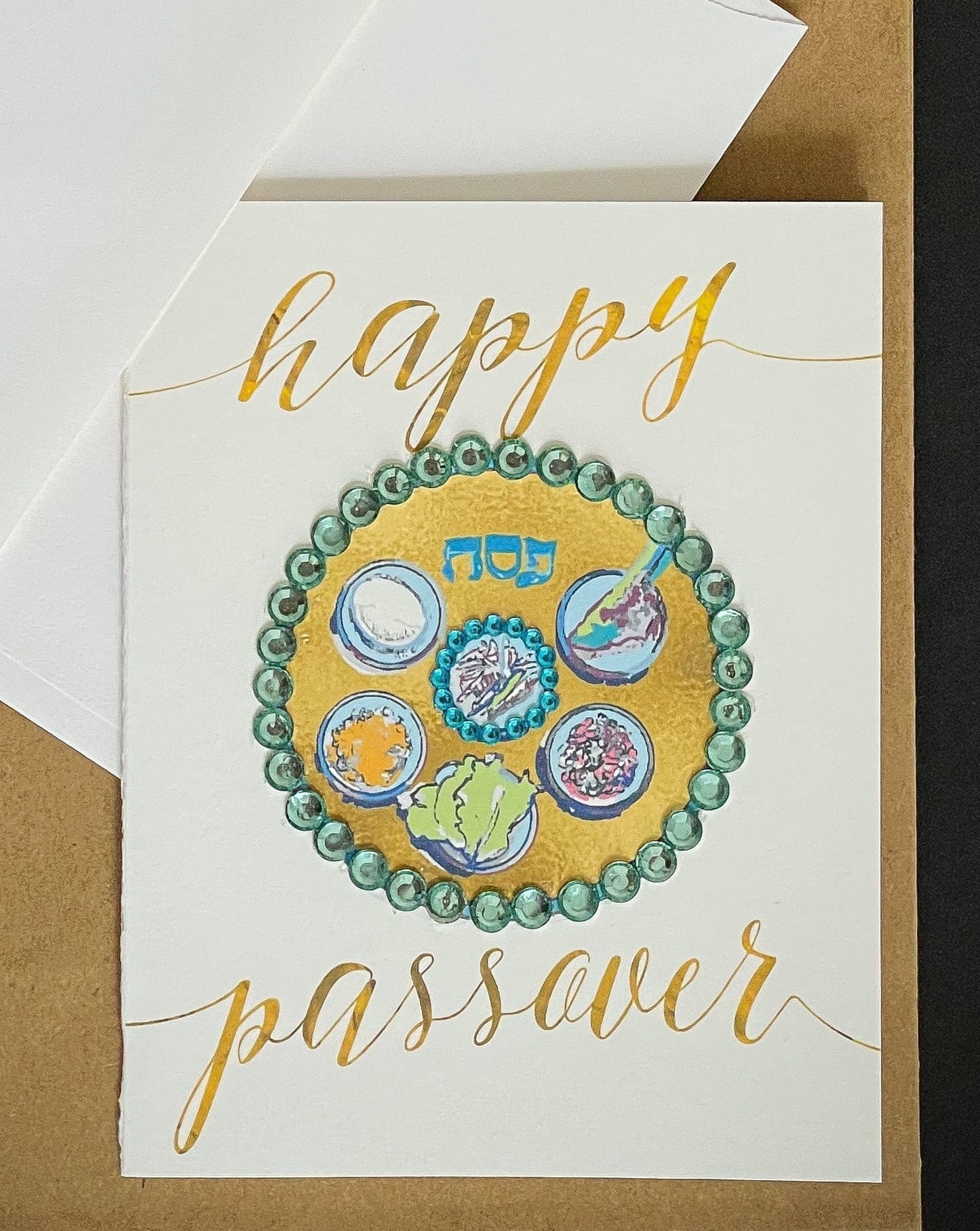 this is a note card on a craft paper gift bag with a white envelope and a black marker , the card has Happy Passover with a decorated gold Sedar plate