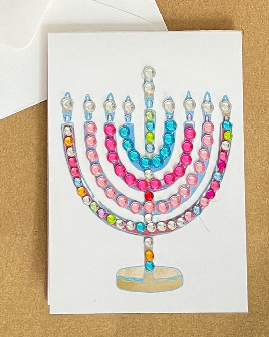 this is a mini note card on a craft paper gift bag with a white envelope and a black marker , the card has a decorated menorah