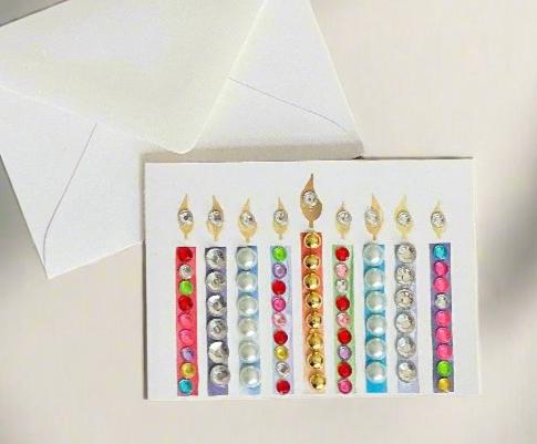 this is a mini note card on a craft paper gift bag with a white envelope and a black marker , the card has a decorated menorah