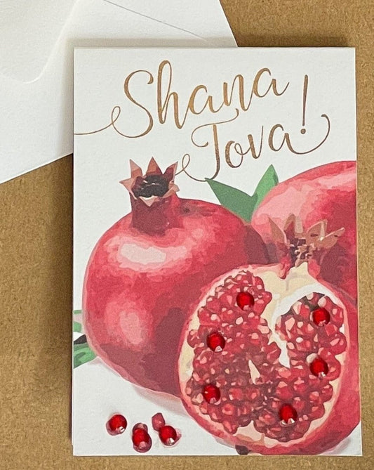 this is a mini note card on a craft paper gift bag with a white envelope and a black marker , the card says Shana Tova in English with a group of pomegranates